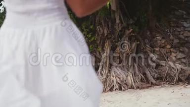 穿着白色衣服和帽子的年轻漂亮女人回头在热带海滩上为自己招手。 慢动作。 3840x2160